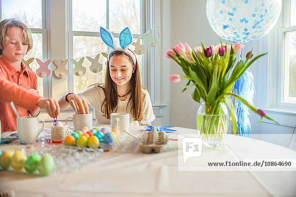 Teenager-Mädchen und Bruder färben hart gekochte Eier für Ostern bei Tisch