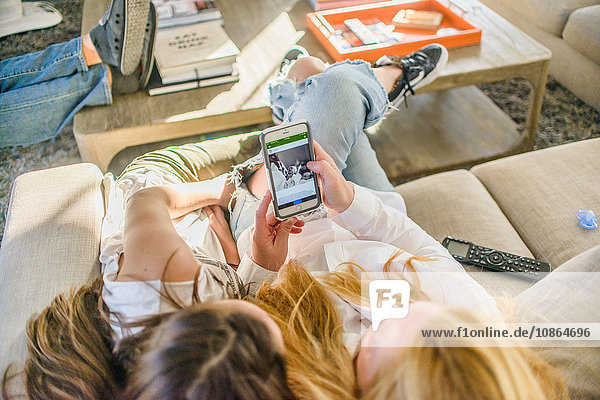 Draufsicht auf Mutter und Teenager-Tochter  die auf dem Sofa sitzen und auf das Neugeborenenfoto auf dem Smartphone schauen
