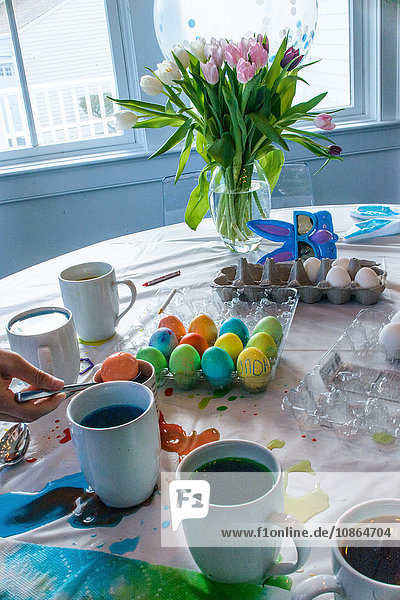 Hand eines Jungen beim Tischdecken  während er Eier für Ostern färbt