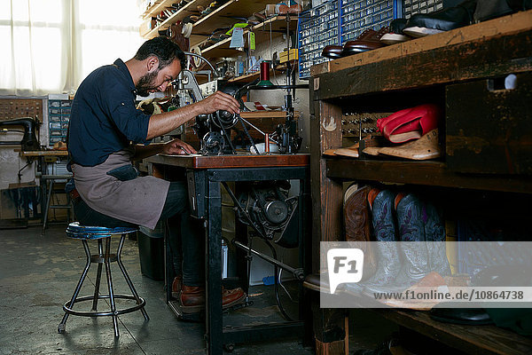 Male cobbler in traditional shoe workshop at sewing machine