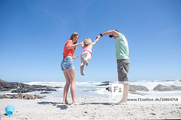 Junges Paar hält und schwingt ein weibliches Kleinkind am Strand  Kapstadt  Südafrika