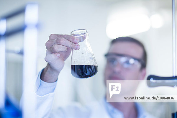 Mittelgroßer erwachsener Mann im Labor  betrachtet Flüssigkeit in Glaskolben
