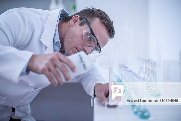 Mann im Labor  der Flüssigkeit in eine Reihe von Reagenzgläsern gießt
