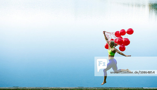 Frau hält einen Haufen roter Luftballons  die in die Luft springen
