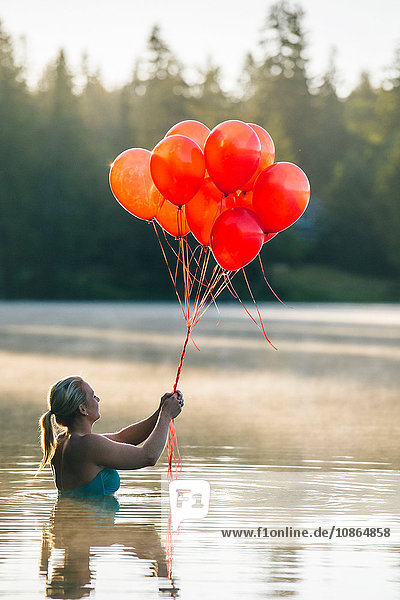 Frau im Wasser hält einen Haufen roter Luftballons
