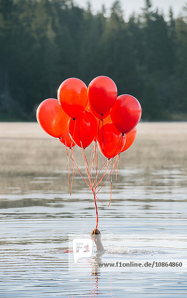 Hand in water holding bunch of red balloons