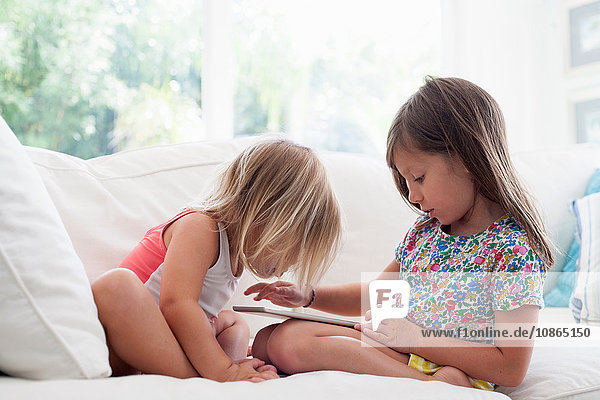 Sisters on sofa using digital tablet