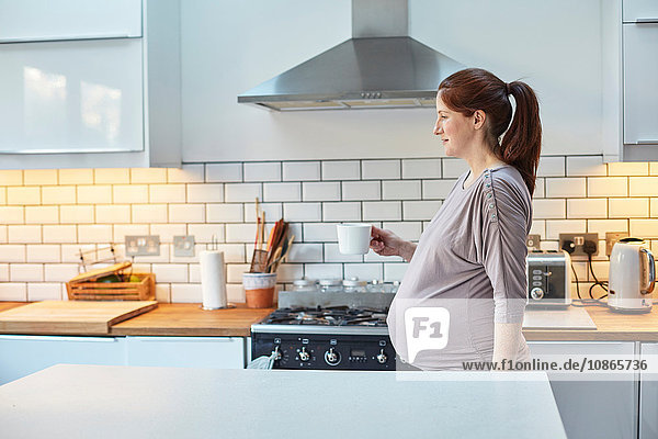 Schwangere Frau in der Küche hält Kaffeetasse