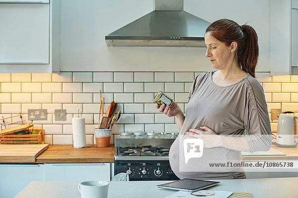 Seitenansicht einer schwangeren Frau in der Küche mit Blick auf Lebensmittelverpackungen