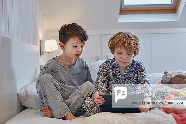 Jungen in Pyjamas mit digitalem Tablett im Bett