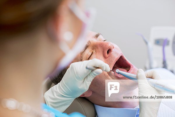 Blick über die Schulter eines Zahnarztes  der eine zahnärztliche Untersuchung am reifen Mann durchführt
