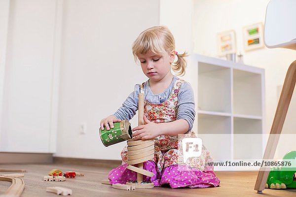 Auf Holzboden kniendes Mädchen spielt mit Spielzeug