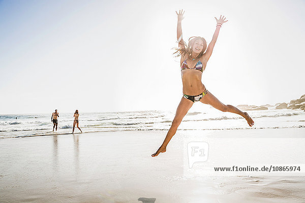 Mid adult woman wearing bikini jumping mid air at beach Cape Town South Africa