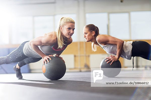 Two female crossfitters doing push ups on medicine ball in gym