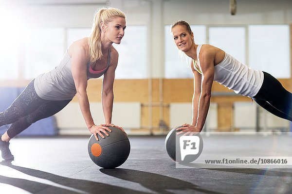 Two female crossfitters pushing up on medicine ball in gym