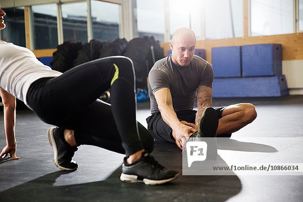 Male and female crossfitters sitting on floor stretching legs