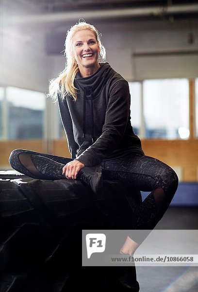 Portrait of mid adult female crossfitter sitting on tyre stack in gym
