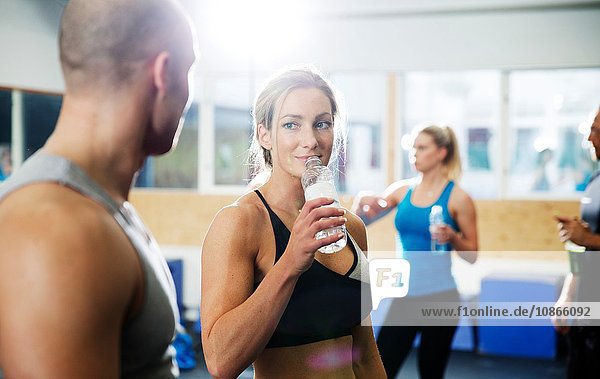 Male and female crossfitters drinking bottled water in gym