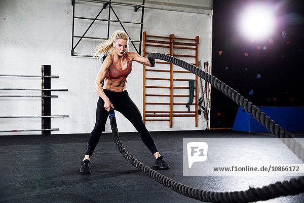 Mid adult female crossfitter using battling ropes in gym