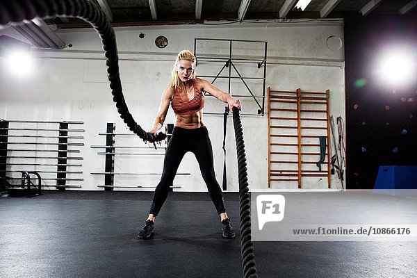 Female crossfitter training with battling ropes in gym