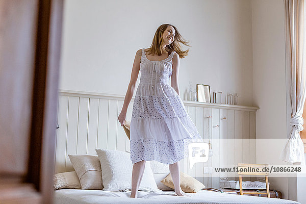 Frau in weißem Kleid springt auf Bett
