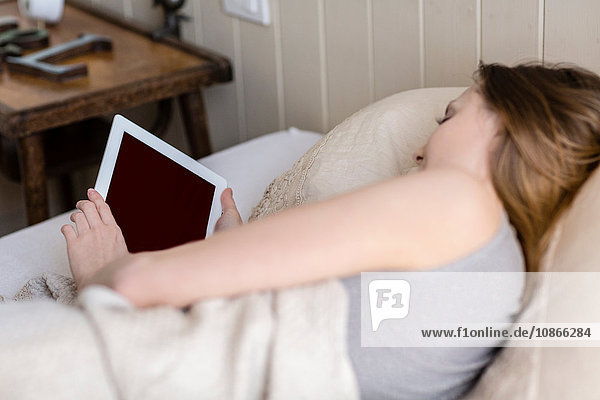 Over the shoulder view of woman lying in bed using digital tablet