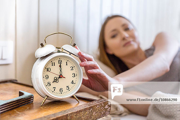 Woman in bed reaching for alarm clock on bedside table