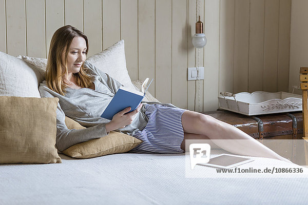 Frau sitzt auf Bett und liest Buch