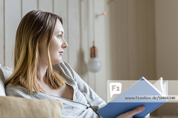 Woman sitting on bed holding book looking away