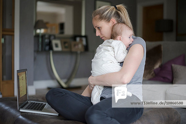 Mutter hält einen kleinen Jungen  während sie einen Laptop benutzt