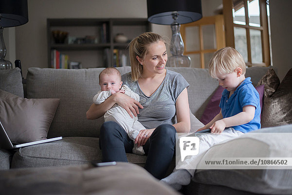 Mother sitting in living room with son and baby boy  son holding digital tablet