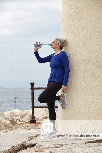 Reife Frau im Freien  an die Wand gelehnt  aus Wasserflasche trinken