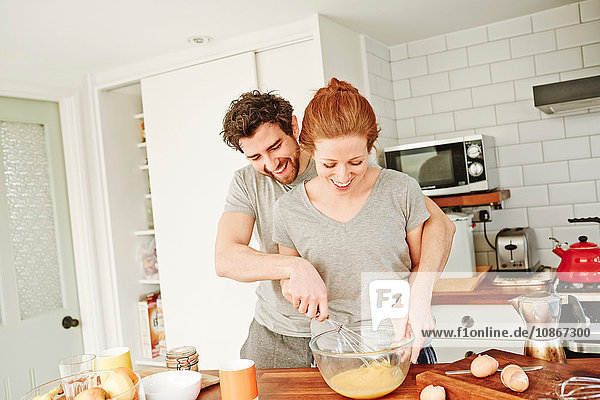 Mid adult couple whisking eggs together at kitchen counter for breakfast