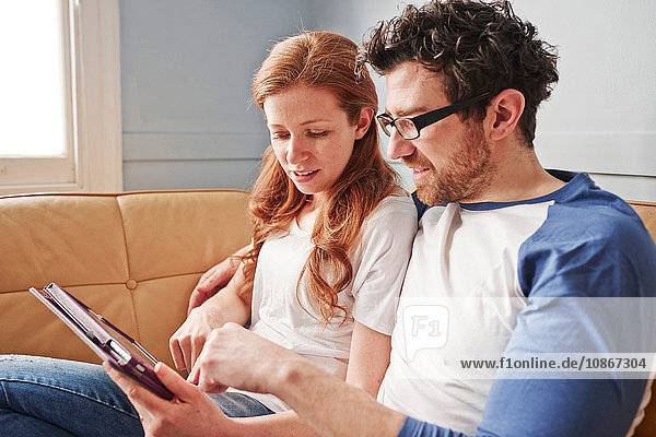 Mittleres erwachsenes Paar entspannt sich auf dem Sofa und schaut auf ein digitales Tablet