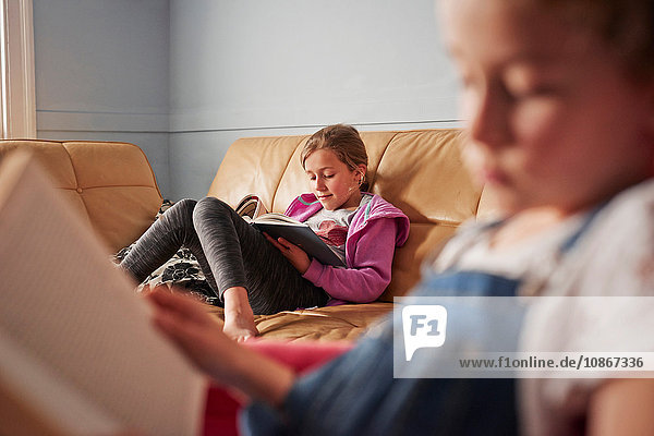 Nahaufnahme eines Mädchens und seiner Schwester beim Lesen von Büchern im Wohnzimmer