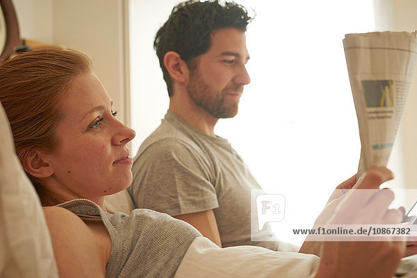 Mittelgroßes erwachsenes Paar liest Einblattdruck im Bett
