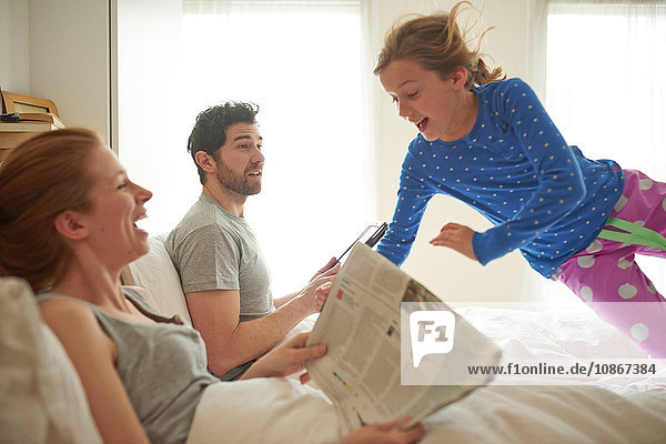 Mittelgroßes erwachsenes Paar liest Einblattdruck  während die Tochter auf das Bett springt