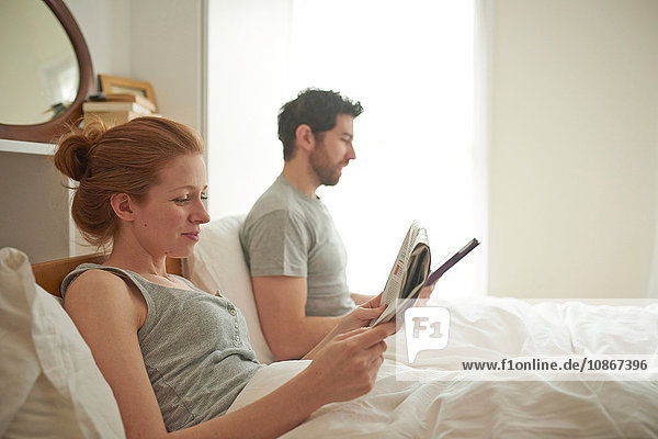 Mittelgroßes erwachsenes Paar liest im Bett digitale Tablette und ein Einblattdokument