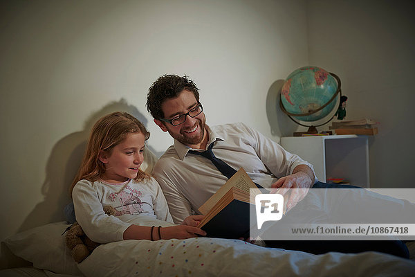 Geschäftsmann liest seiner Tochter zur Schlafenszeit ein Märchenbuch vor