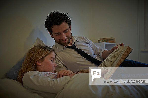 Geschäftsmann liest seiner schlafenden Tochter zur Schlafenszeit ein Märchenbuch vor