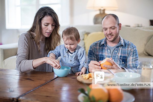 Eltern essen mit dem Baby zu Mittag  schälen Orange