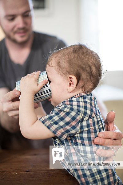Father helping baby boy to drink from mug