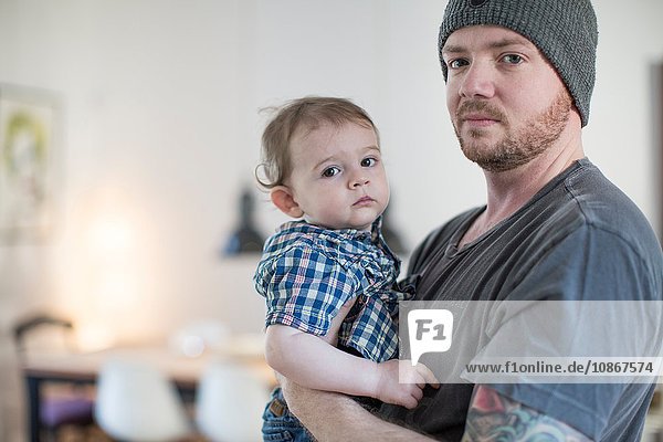 Father wearing knit hat holding baby boy looking at camera