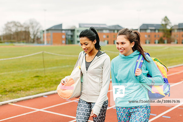 Zwei junge Frauen laufen auf der Laufbahn und tragen Sporttaschen