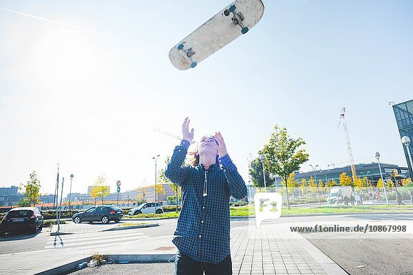 Junge männliche städtische Skateboarder werfen Skateboard mitten in der Luft