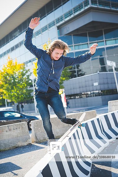Junger männlicher Stadtskateboarder  der auf einer Betonbarriere balanciert.