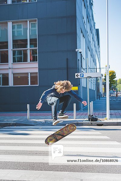 Junger männlicher Skateboardfahrer beim Skateboard-Sprung auf dem Fußgängerüberweg