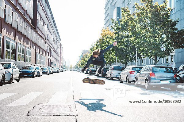 Junge männliche Skateboarder aus der Stadt springen in der Luft auf dem Fußgängerüberweg