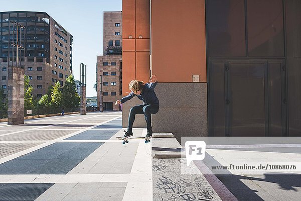Young male skateboarder skateboarding up urban step