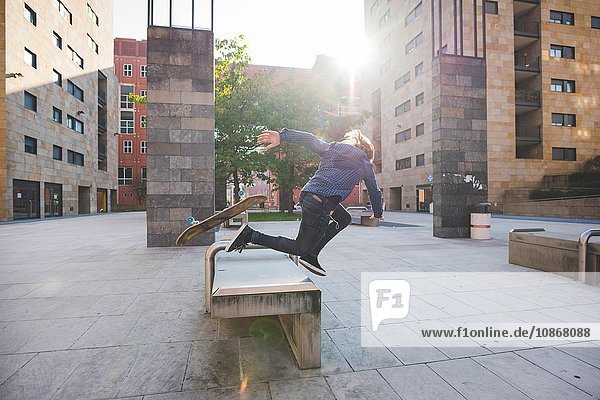 Junger männlicher Skateboarder  der beim Skateboarden auf dem Sitz der Stadthalle kopfüber fällt